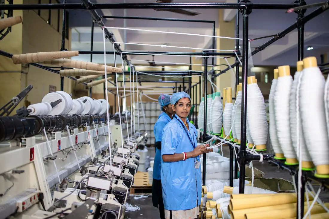 Textile workers operating machinery beside spools of thread